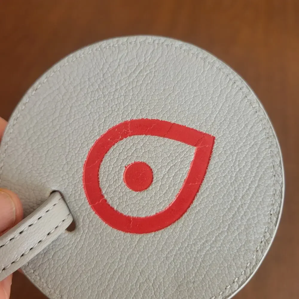 Round textured leather luggage tag in light grey with a red map
